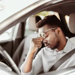 Erschöpfter Mann mit Brille reibt sich die Augen, während er im Auto sitzt. Die lange Fahrt ermüdet ihn.