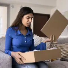 Femme déçue ouvrant un colis, découvrant un produit non conforme à la commande. Elle exprime son mécontentement.