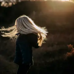 Dziecko z rozwianymi blond włosami w świetle zachodzącego słońca.
