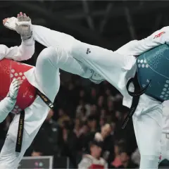Två taekwondo-utövare i strid. Den ena med röd väst och hjälm, den andra med blå väst och hjälm. Båda utför sparkar.