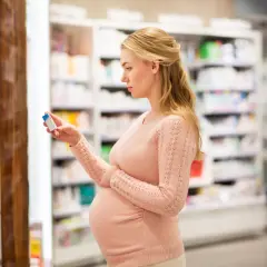 Ciężarna kobieta wybiera w aptece suplement, być może Acidum Folicum Richter, dla zdrowia mamy i dziecka.