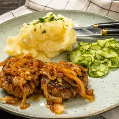Två saftiga pannbiffar i ugn med karamelliserad lök, serverade med krämigt potatismos och gurksallad. En klassisk svensk rätt.
