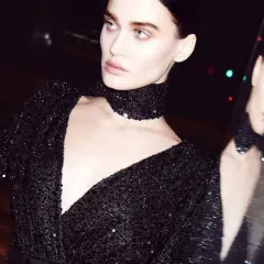 Modelka w czarnej sukience z cekinami i chokerem, odbijająca się w lustrze.