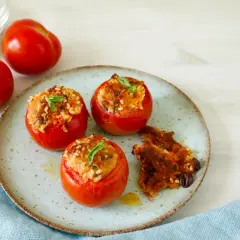 Pomodori ripieni tonno e riso, guarniti con basilico, su un piatto con un contorno croccante.