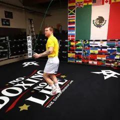 Boxer in yellow shirt doing a boxing jump rope workout in a ring decorated with flags.