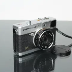 A vintage silver Olympus 35 ECR rangefinder camera with a black textured grip sits on a reflective surface.