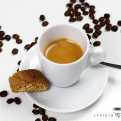 Ein weißer Becher mit Kaffee, daneben ein Cantuccini und Kaffeebohnen. Das ist ein Kaffee Lungo, ein längerer Espresso.