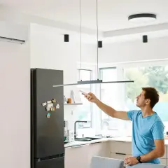 Mężczyzna z pilotem w ręku obsługuje klimatyzację w nowoczesnej kuchni.