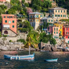 Des maisons colorées s'accrochent à la falaise sur la **riviera italienne où aller**. Des bateaux flottent paisiblement dans l'eau bleue.