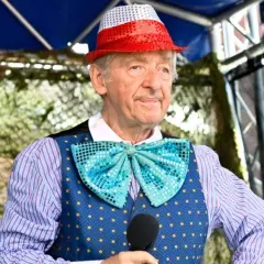 Uśmiechnięty Andrzej Rosiewicz w cekinowym kapeluszu i muszce, trzymający mikrofon. Wiek artysty to 80 lat.