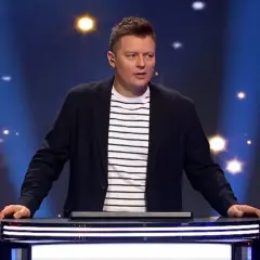 Prowadzący program "Jaka to melodia?" w eleganckim stroju, zastanawia się, ile zarabia zawodowy gracz w Jaka to melodia za jeden odcinek.