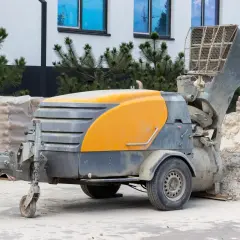 Mobilna maszyna do betonu, gotowa do pracy nad posadzkami z miksokreta. Obok piasek i materiały budowlane.