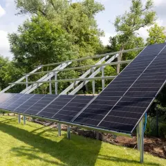 Instalacja paneli fotowoltaicznych na metalowym profilu montażowym pv. Panele ustawione na trawniku, w tle drzewa i niebo.