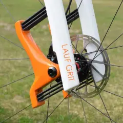 Close-up of a bright orange and white Lauf Grit fork on a bicycle wheel, ready for adventure.