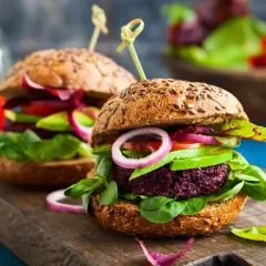 Zwei saftige vegane Burger mit Rote-Bete-Patty, Avocado, Tomate und Zwiebeln auf Vollkornbrötchen – perfekt für vegan zunehmen!