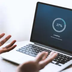 Verzweifelte Person schaut auf Laptop, auf dem "Loading... 27%" steht. Windows startet nach Update nicht mehr.