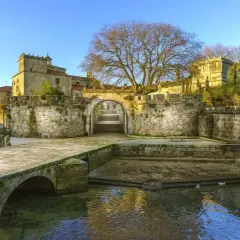 El pazo Vista Alegre, con su puente de piedra y río, se alza majestuoso bajo un cielo azul.