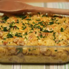 Zapiekanka makaronowa z boczkiem i serem, posypana natką pietruszki, w szklanym naczyniu.