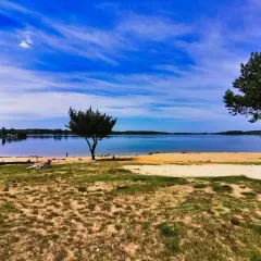 Słoneczny dzień nad jeziorem Pławniowice. Ludzie odpoczywają na piaszczystej plaży, ciesząc się błękitem nieba i spokojną wodą.