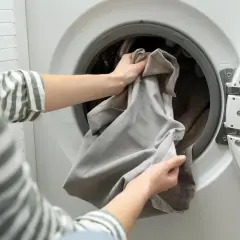 Hände legen Gardinen in die Waschmaschine. Die Frage "Gardinen waschen wieviel Grad?" ist wichtig für die richtige Pflege.