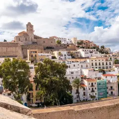 Widok na zabytkowe miasto z katedrą na wzgórzu. Białe domy, zielone drzewa i błękitne niebo. To właśnie tutaj jest Ibiza.