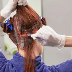 Persona se tiñe el pelo en casa, aplicando tinte con un pincel.