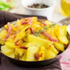 Patatas al microondas con trocitos de bacon crujiente y romero fresco, servidas en una sartén metálica.