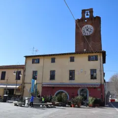 Torre dell'orologio in un tranquillo cascina paese, con negozi e gente che passeggia nella piazza.