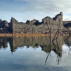 Ruinas de piedra emergen del agua en el embalse de Portodemouros, reflejando su silueta en la calma superficie.
