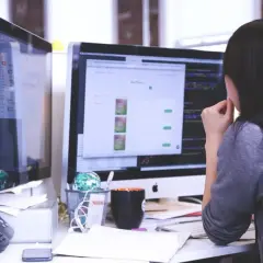 Une femme travaille sur un ordinateur dont l'écran, de la taille d'un écran 24 pouces, affiche un site web de produits.