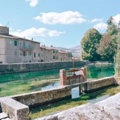 Un canale d'acqua cristallina attraversa un borgo con case antiche, ricordando i pittoreschi **paesi vicini al Monte Amiata**.