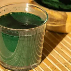 Ein Glas grüner Chlorella-Drink steht auf einem Bambusteller. Manche berichten von leichten Chlorella Nebenwirkungen wie Verdauungsbeschwerden.