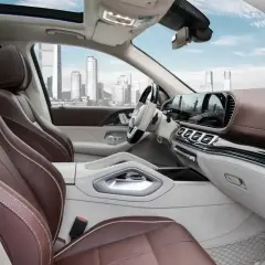 Wnętrze luksusowego **Mercedes GLS 2025** z brązową skórzaną tapicerką i nowoczesnym panelem. Widok na miasto przez panoramiczny dach.