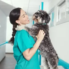 Veterinaria sonríe mientras abraza a un perro, ajenos a los ladridos de perros que se oyen en el pasillo.