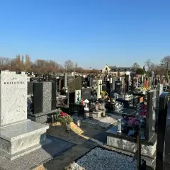Nagrobek z krzyżem i napisem "Ś.P. ROSŁoniec" na tle cmentarza.
