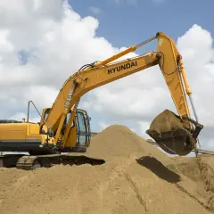 Żółta koparka Hyundai pracuje na placu budowy, przesypując piasek. Sprawdź aktualną pospółka cena.