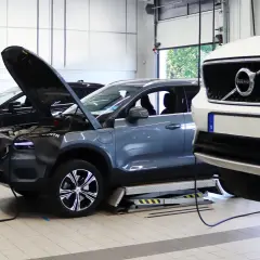 Flera Volvo-bilar, inklusive en vit XC40 och en grå elbil, på verkstad för volvo classic service. Motorhuvar öppna för inspektion.
