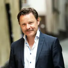 Kasper Sulocki, en man med mustasch, bär en mörkblå rutig kavaj och vit skjorta i en gränd.