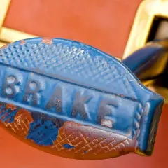 Stary, niebieski uchwyt hamulca z napisem "BRAKE". Rdza i odpryski farby sugerują, jaki smar do prowadnic hamulcowych byłby potrzebny.