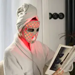 Person med handduk på huvudet och en led mask ansikte läser en bok i en morgonrock.