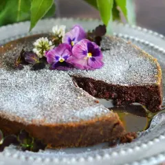 En saftig tårta med chokladpudding, pudrad med florsocker och dekorerad med violer och klöver. En bit är uppskuren.