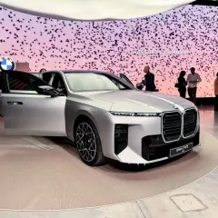 Elegancki, srebrny BMW i7 M70 G10 z otwartymi drzwiami na wystawie. Tło zdobią stylizowane ptaki i logo BMW.