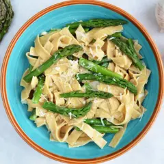 Makaron tagliatelle z zielonymi szparagami i startym parmezanem w niebieskiej misce.