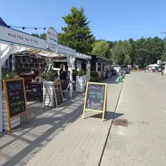 Dębki promenada: lokal Belona zaprasza na muzykę na żywo i koncerty. W tle widać letnie ogródki i spacerujących ludzi.