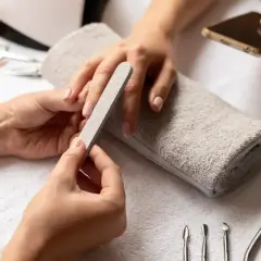 Dłonie przygotowują się do zabiegu, jak zdjąć paznokcie żelowe. Pilniczek delikatnie modeluje paznokieć, a obok leżą narzędzia do manicure.