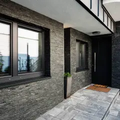 Nowoczesny dom z kamienną elewacją i czarnymi oknami. Świetny pomysł na elewację domu, który nadaje mu elegancki i minimalistyczny charakter.