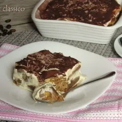 Una fetta di tiramisù classico, con savoiardi inzuppati nel caffè e crema al mascarpone, spolverato di cacao e scaglie di cioccolato. La ricetta del tiramisù è un classico intramontabile.