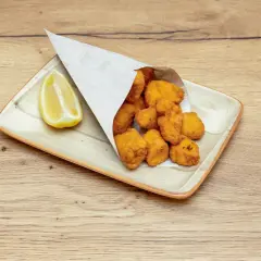 Crujientes trozos de cazon en adobo, servidos en cucurucho de papel, acompañados de una rodaja de limón.