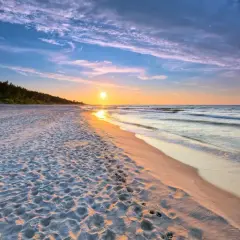 Zachód słońca nad piaszczystą plażą, z widokiem na las i morze. Idealne miejsce na spacer po polskim wybrzeżu, w jednej z urokliwych miejscowości.