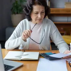Kobieta analizuje dokumenty, zastanawiając się, czy odprawa emerytalna jest opodatkowana. Na biurku laptop, kalkulator i notatnik.